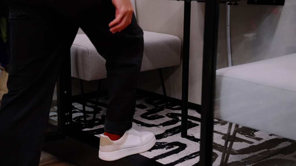 Person wearing white sneakers and red socks, standing on a black-and-white patterned rug beside modern furniture.
