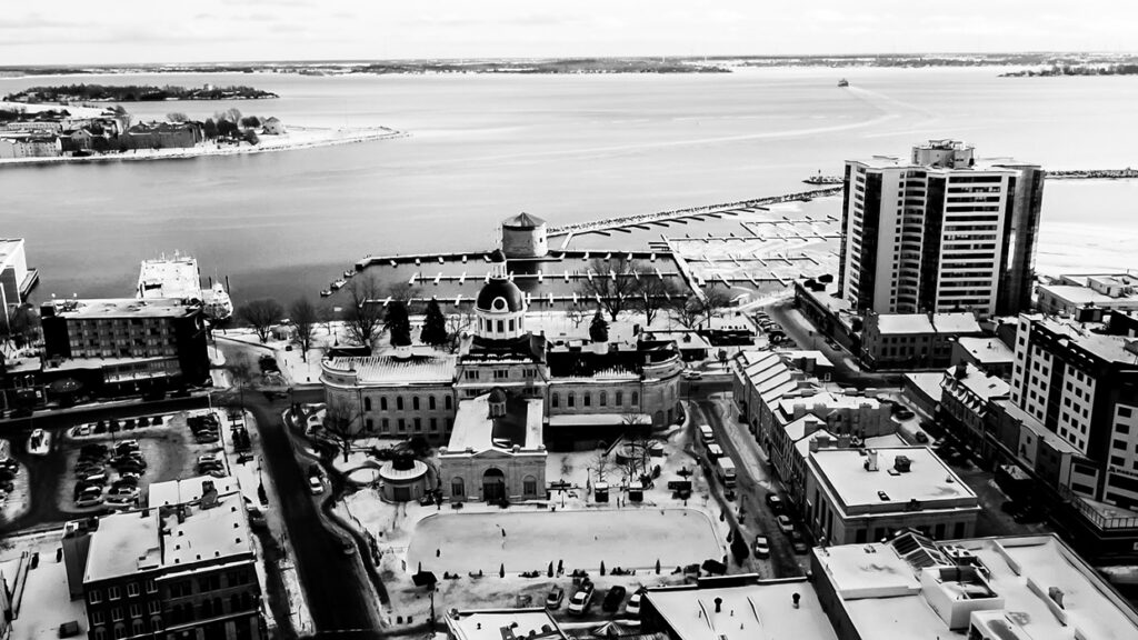 Aerial view of a coastal city with a prominent domed building at the center and a marina along the water's edge in the background.