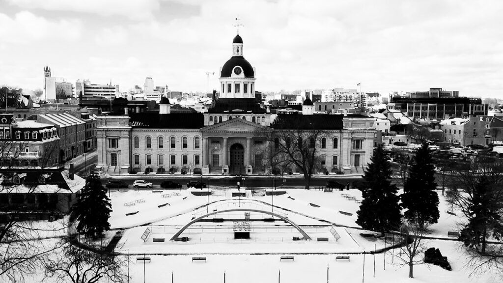 Winter cityscape featuring a grand neoclassical building with a large central dome, set behind a snow-covered plaza and park arches.
