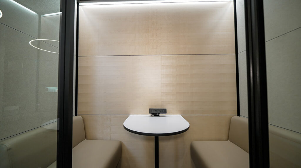 Private office pod with a white semicircular table and beige built-in benches inside a glass-walled booth