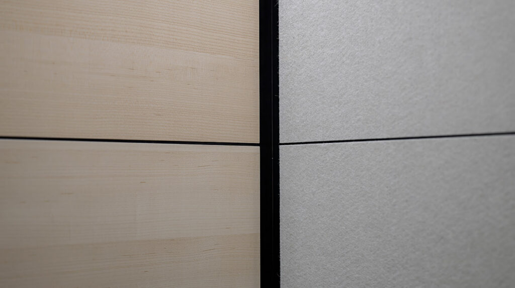 Close-up of a corner where light wood paneling meets a gray textured wall with a black vertical seam in the middle.