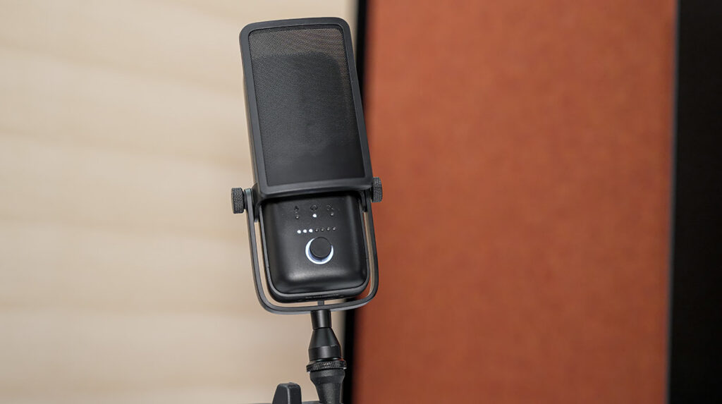 Black studio microphone mounted on an adjustable stand, with a circular LED indicator near the base.