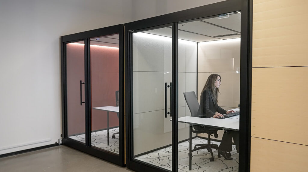 Woman seated at a white desk inside a glass-walled office, typing on a keyboard.