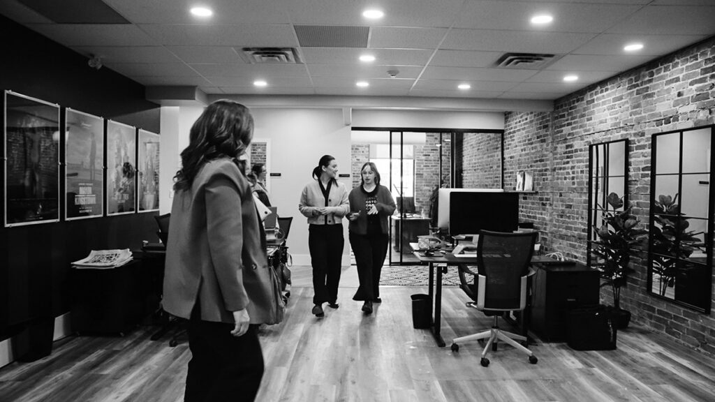 Three colleagues walking through a modern office with brick walls and glass partitions in the background.